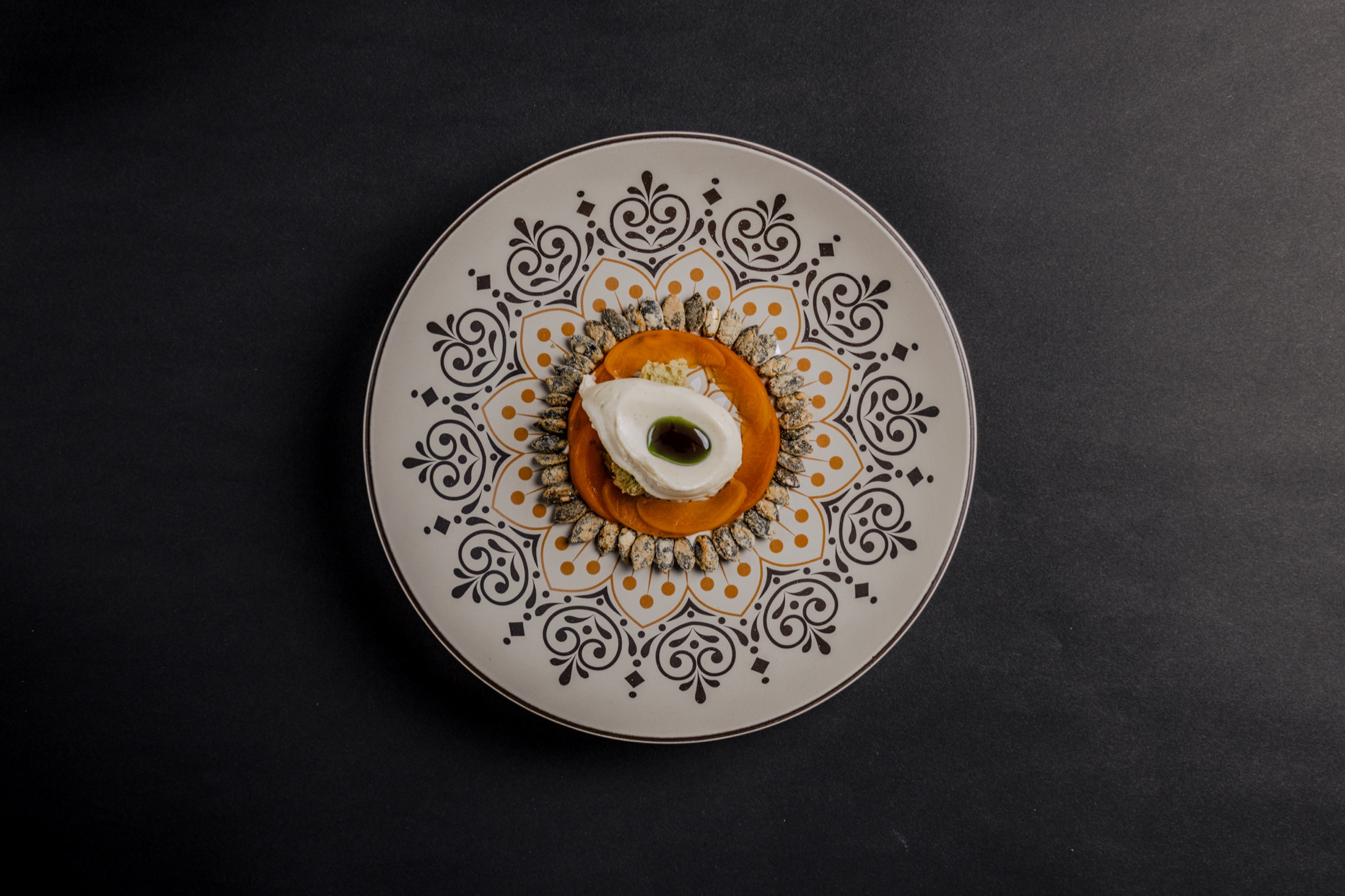Gericht auf ornamentiertem Teller mit oranger Creme